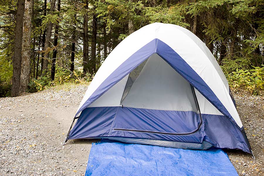 Blue tent on gravel with tarp in front and woods in background