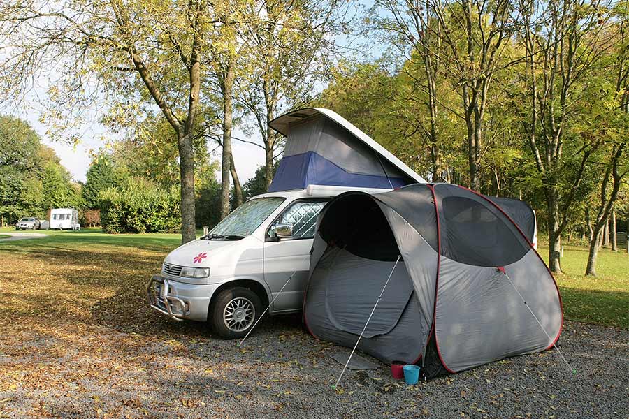 White van with pop up and a gray tent beside it at a campsite