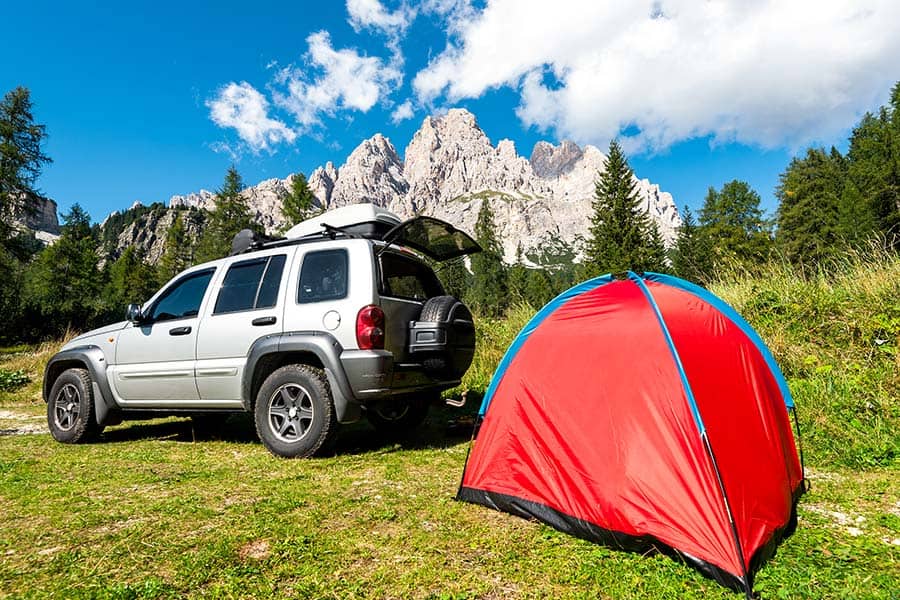 Gray SUV parked beside a red tent in a mountain landscape