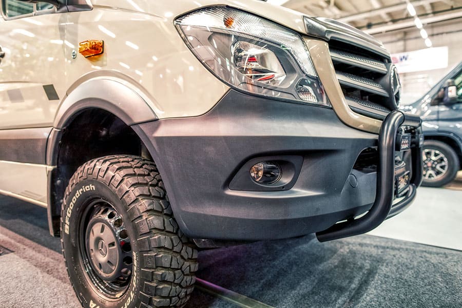 Closeup of the front bumper and tire of a tan Mercedes Benz van