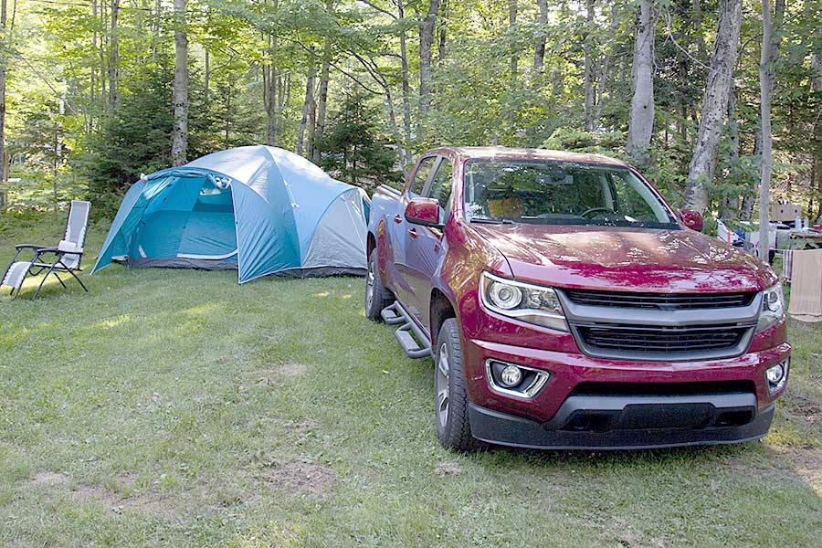 Red truck parked beside a blue tent in a wooded area