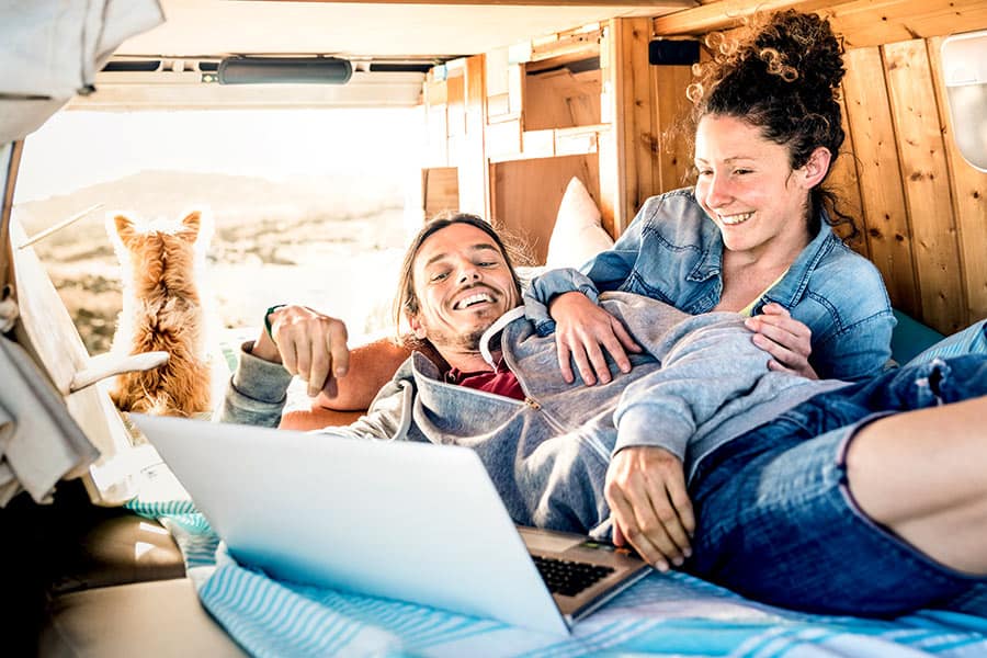 Couple in the back of a van on a bed surfing the internet