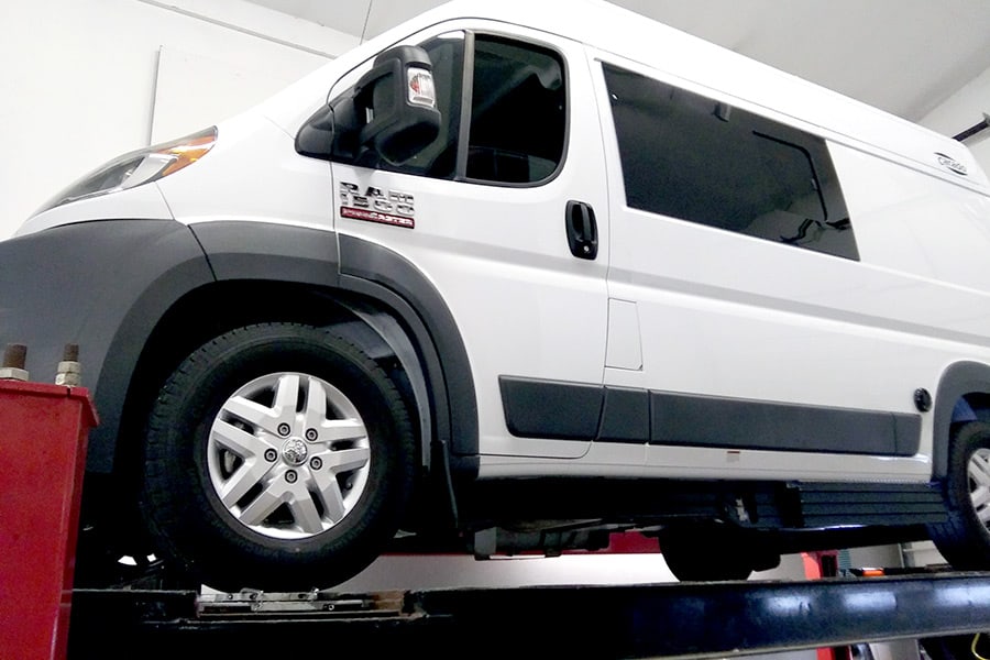 White Class B RV on a lift at a dealer repair center