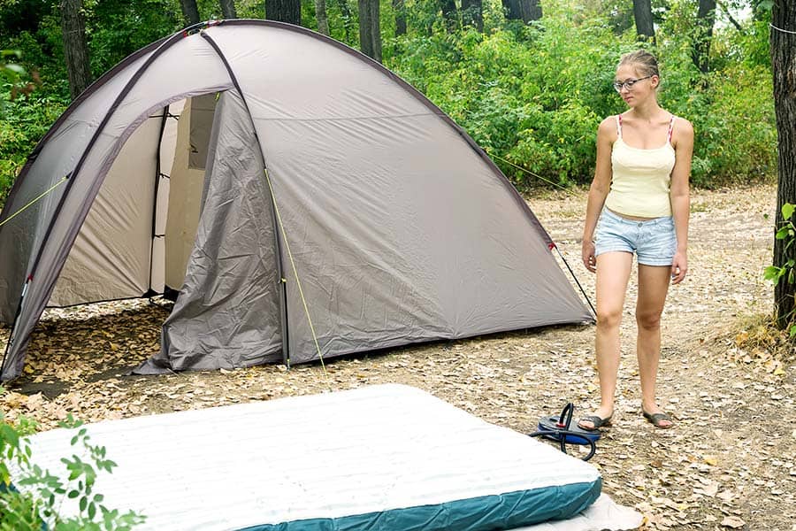 Woman pumping up air mattress outside of tent
