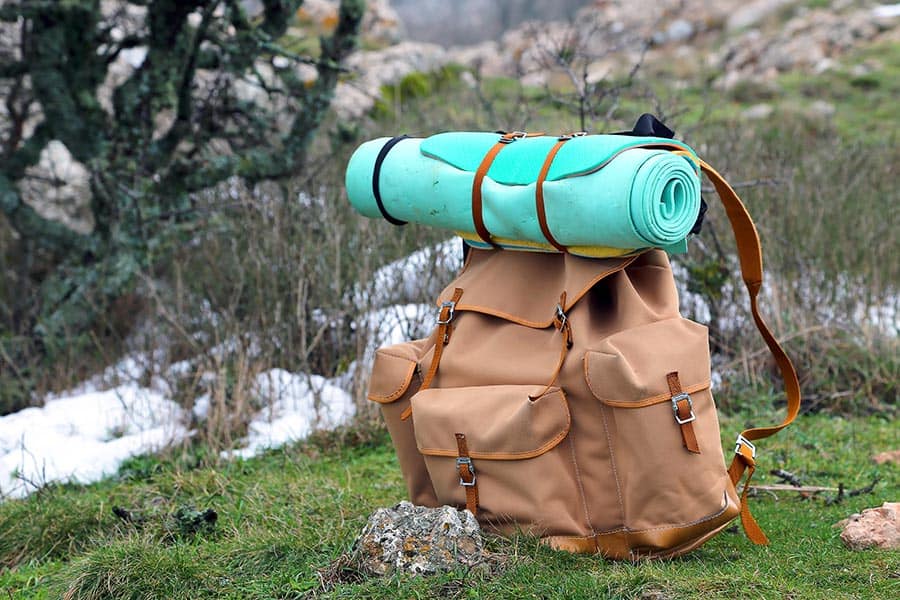 Brown backpack with sleeping roll on top setting in the grass