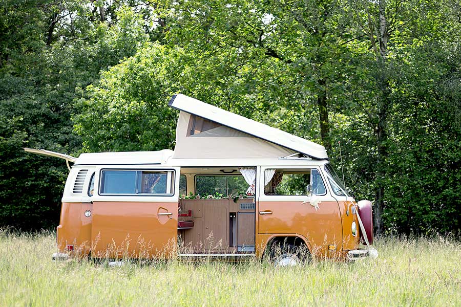 Orangish VW with pop top up in a field