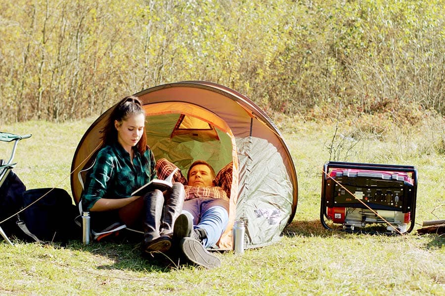 Couple in a small tent with a generator outside on a sunny day