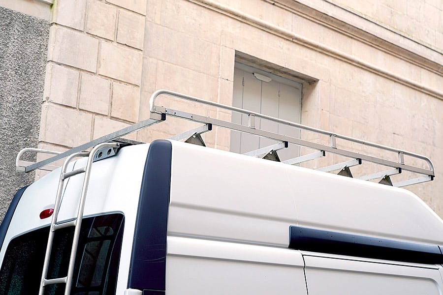 White van with ladder on back and a roof rack parked in front of a building