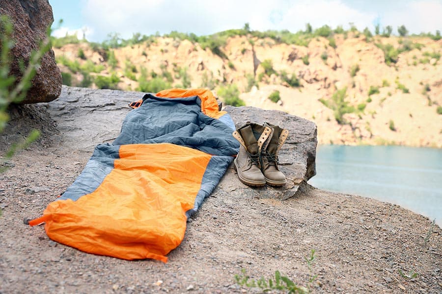 Orange and gray sleeping bag on the ground with boots beside it