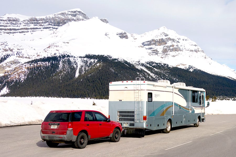 RV towing red vehicle with snowy mountains in the background