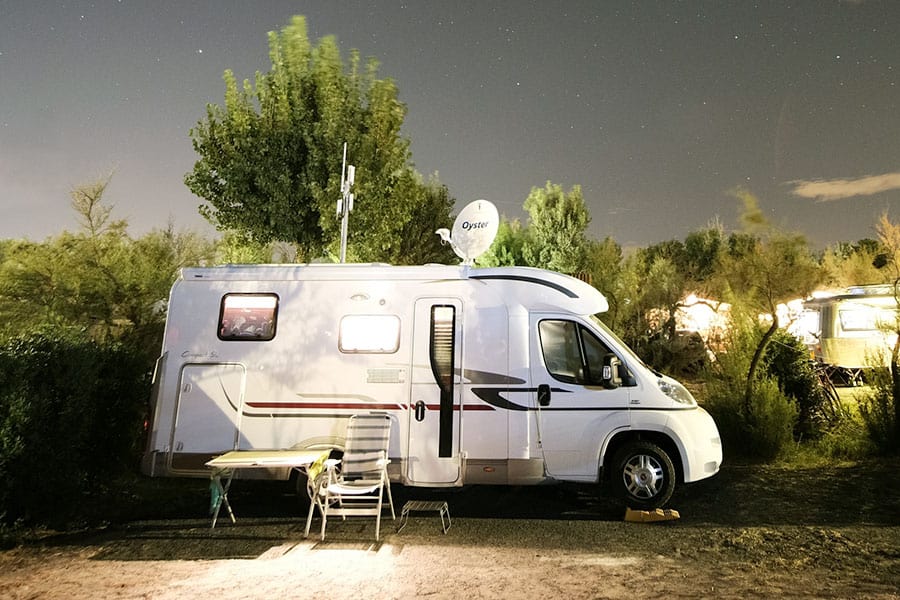 White camper van with chair and table beside it parked in a campground