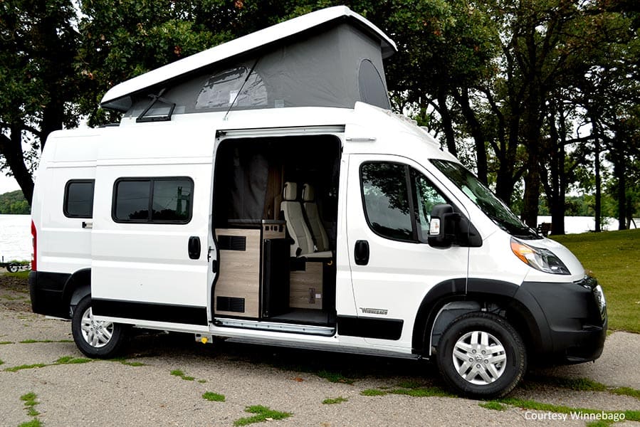 White Class B RV with the pop top up parked near trees