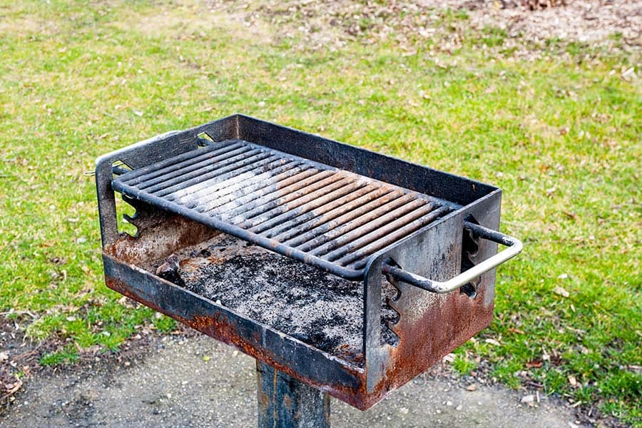 A rusty BBQ grill with charcoal remains in the bottom at a state park