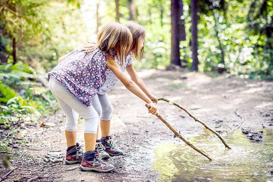 Two girls playing with sticks on puddle of water