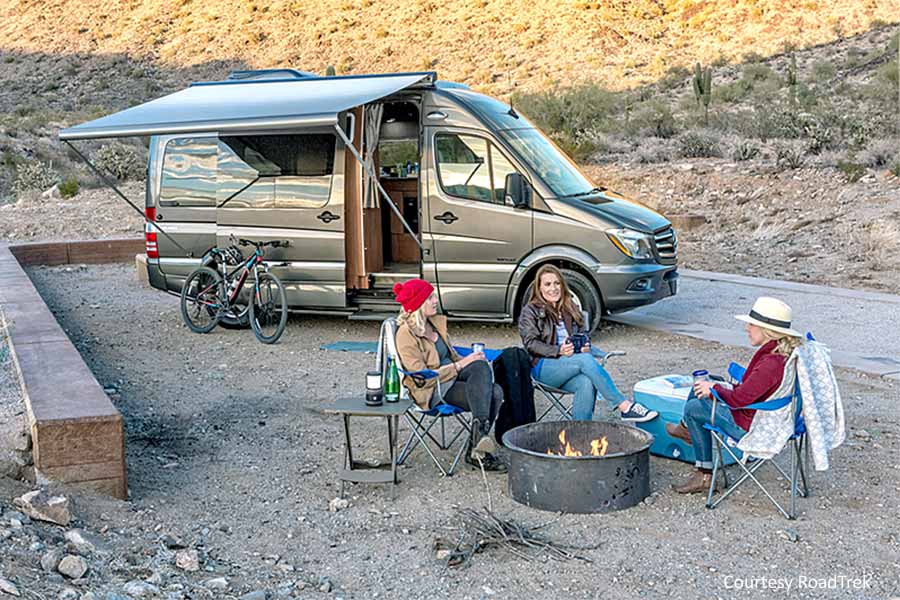 Women sitting around campfire at campsite, Roadtrek camper van in background