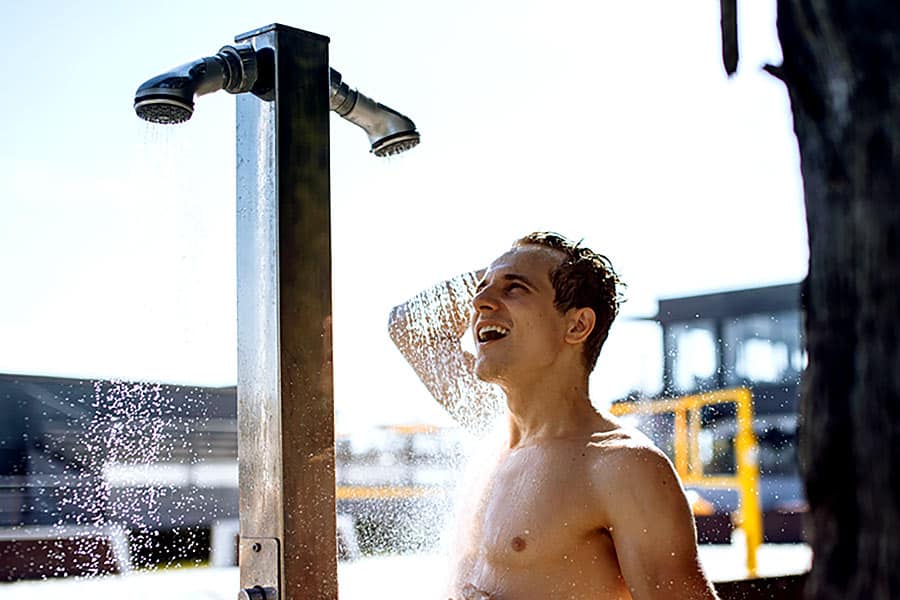 Man at beach using shower to wash off sand