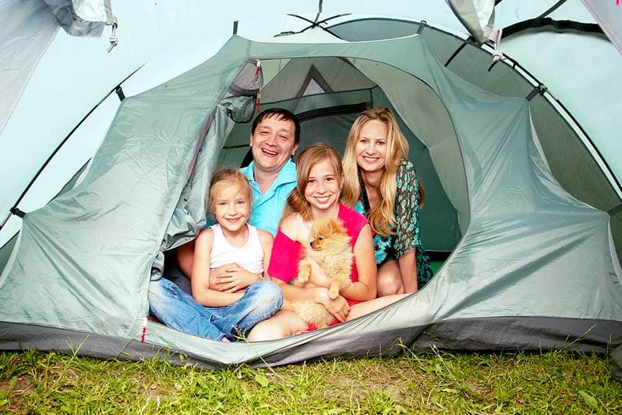 Family sitting in tent opening with small brown dog