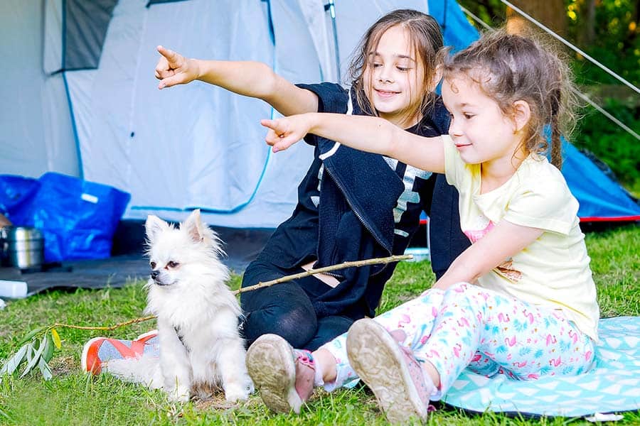 Girls sitting on ground beside tent with small white dog