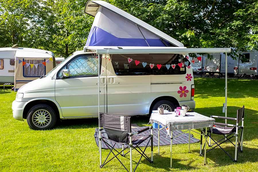 Table and chairs in front of pop top camper van at campground