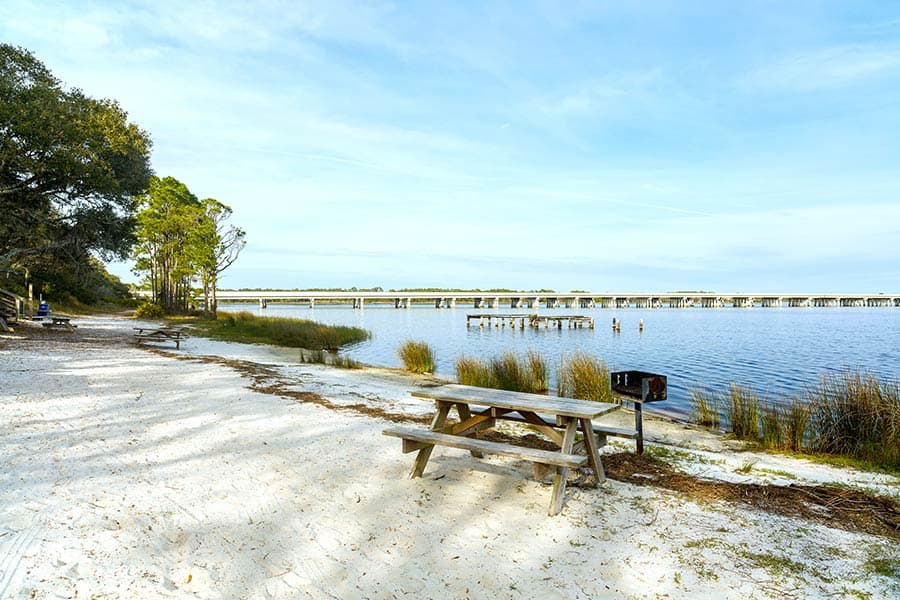 Picnic tables on sandy beach, bridge in background