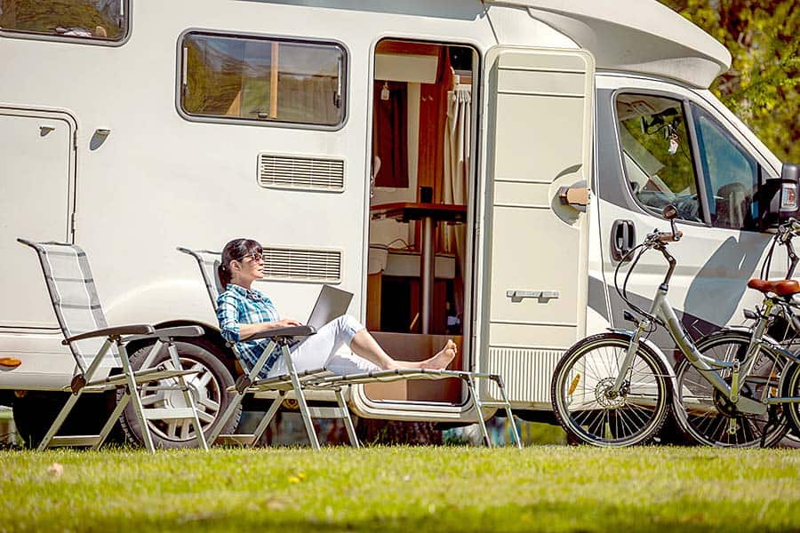 Woman sitting on chair beside camper van working on computer