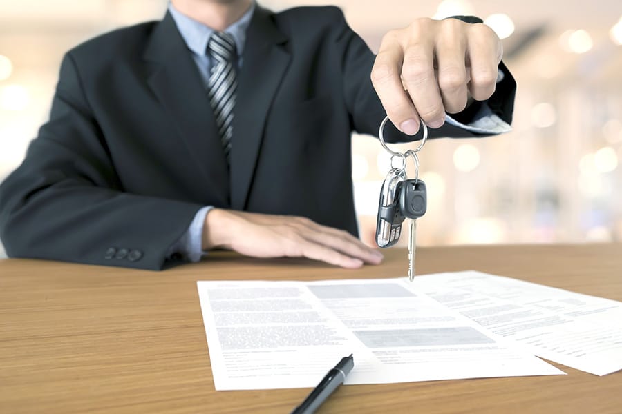 Man sitting at desk handing over keys to vehicle with loan paperwork on desk