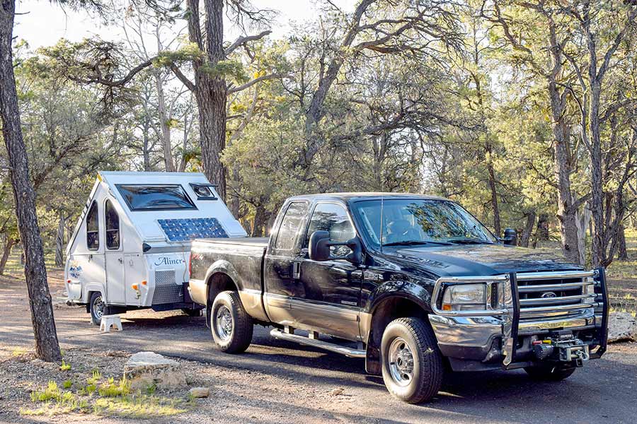 Dark colored truck parked in front of a small camper trailer at campground