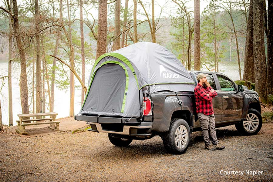 Man leaning against a dark colored truck with a Napier truck tent in the bed