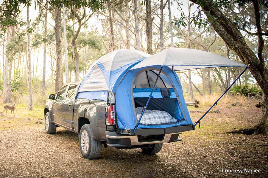 Blue truck tent set up in back of pickup truck parked in the woods