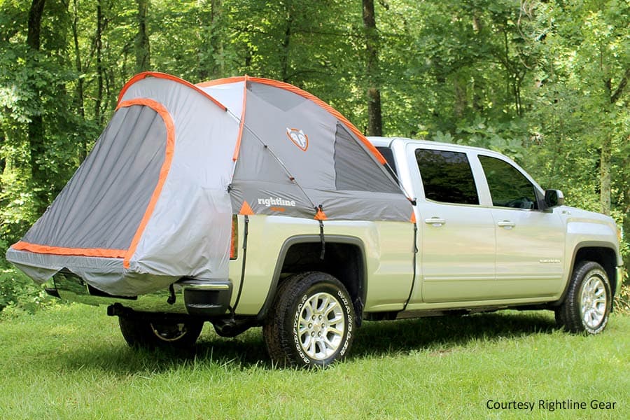 Silver truck with truck tent in bed parked in a wooded location