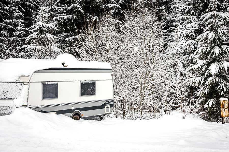 Parked camper trailer covered with snow, snow sticking to trees