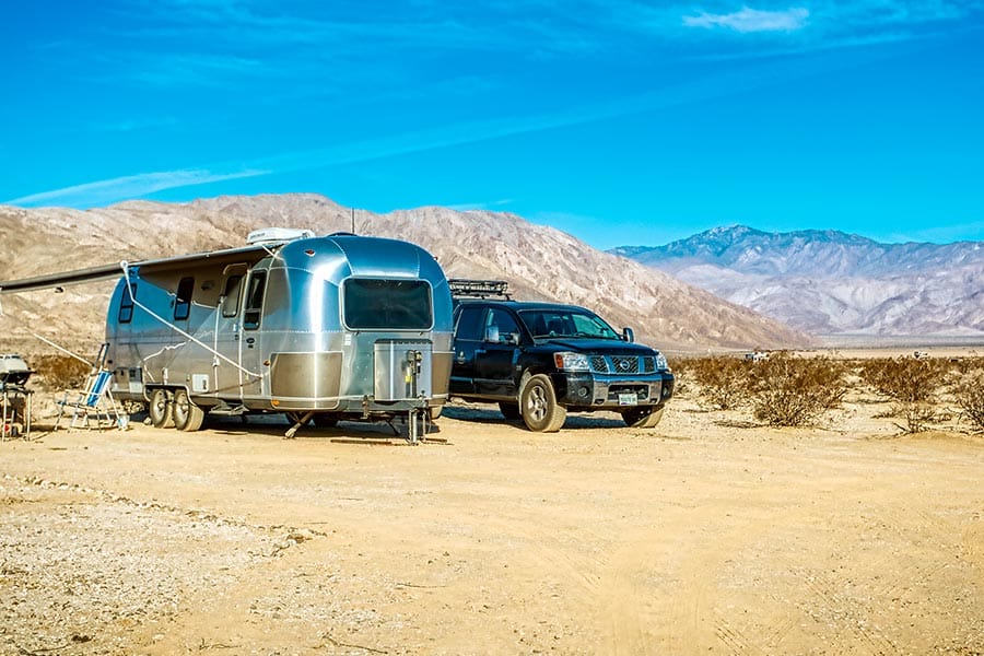 Silver camper trailer with dark colored truck parked beside it