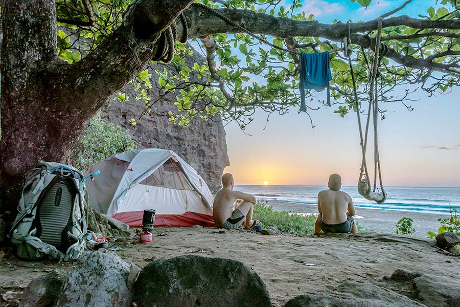 Two young men sitting by tent on beach