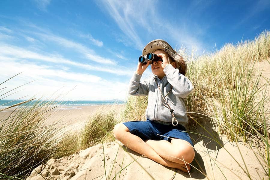 Boy sitting on beach looking at birds through binoculars