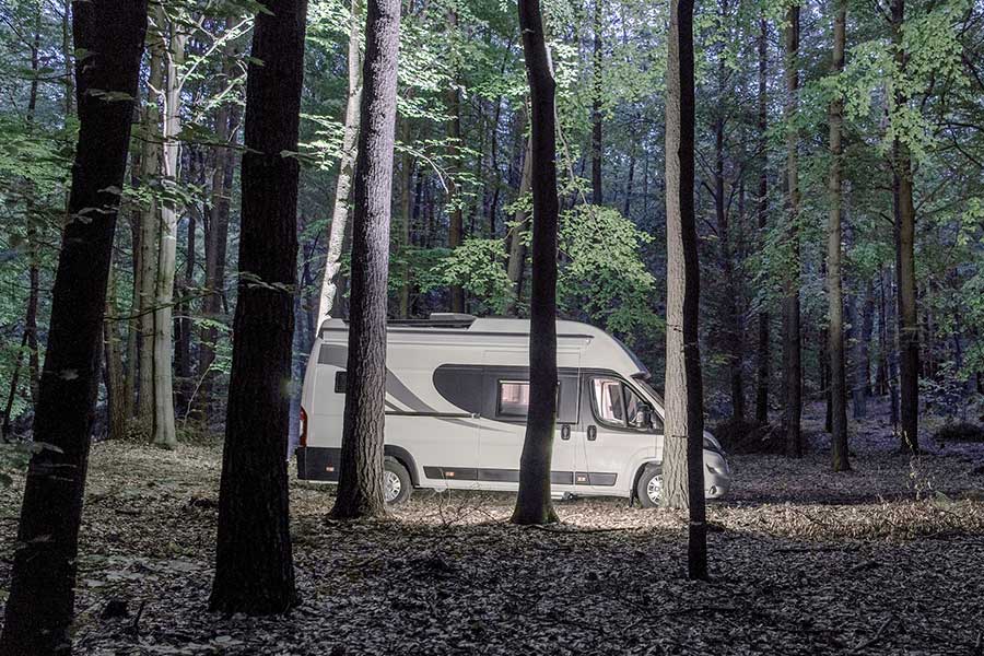 RV parked in the forest among the trees at nightfall