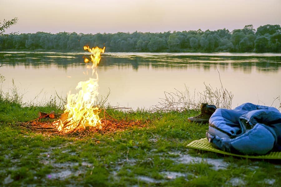 Campfire and sleeping bag on river bank