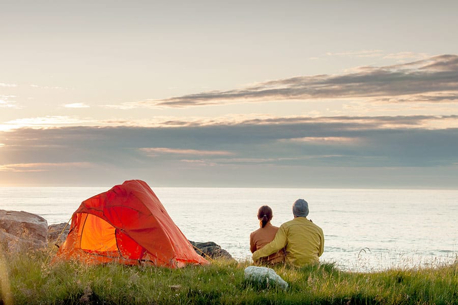 Couple sitting by orange tent overlooking lake