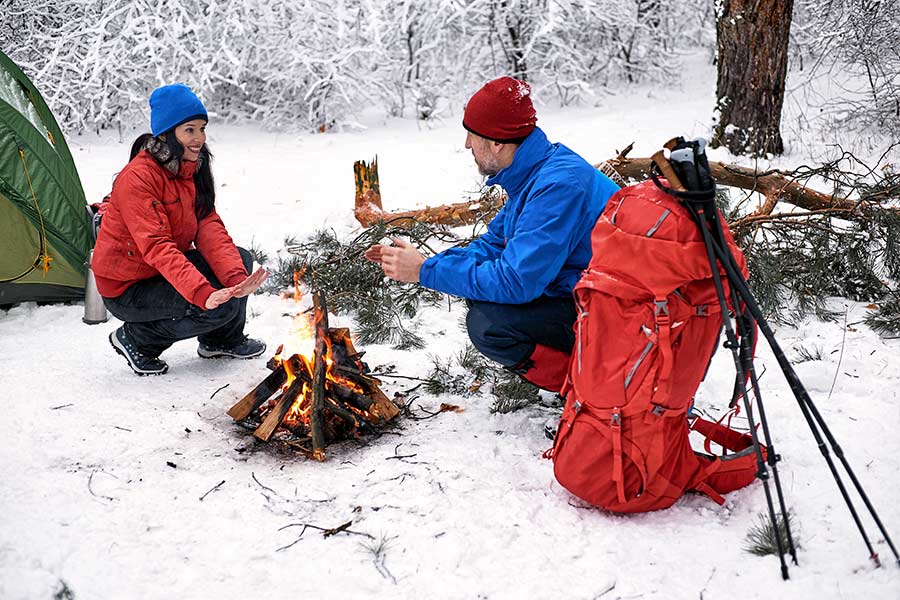 Couple winter camping getting warm by campfire