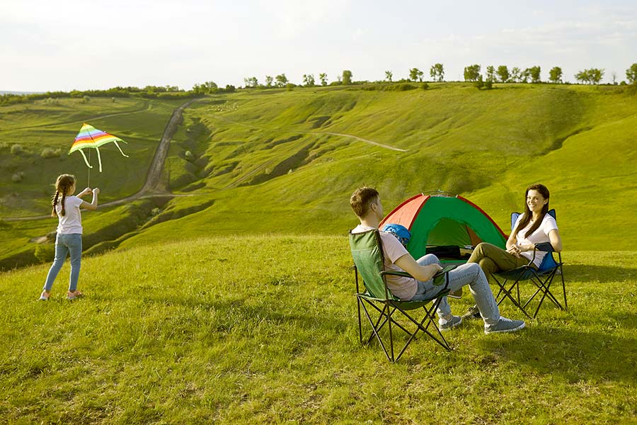 Parents relaxing while daughter flies kite