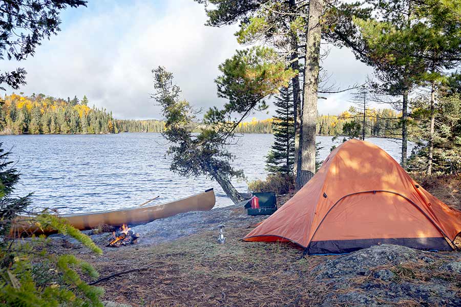 Orange tent by lake, campfire and canoe on shore