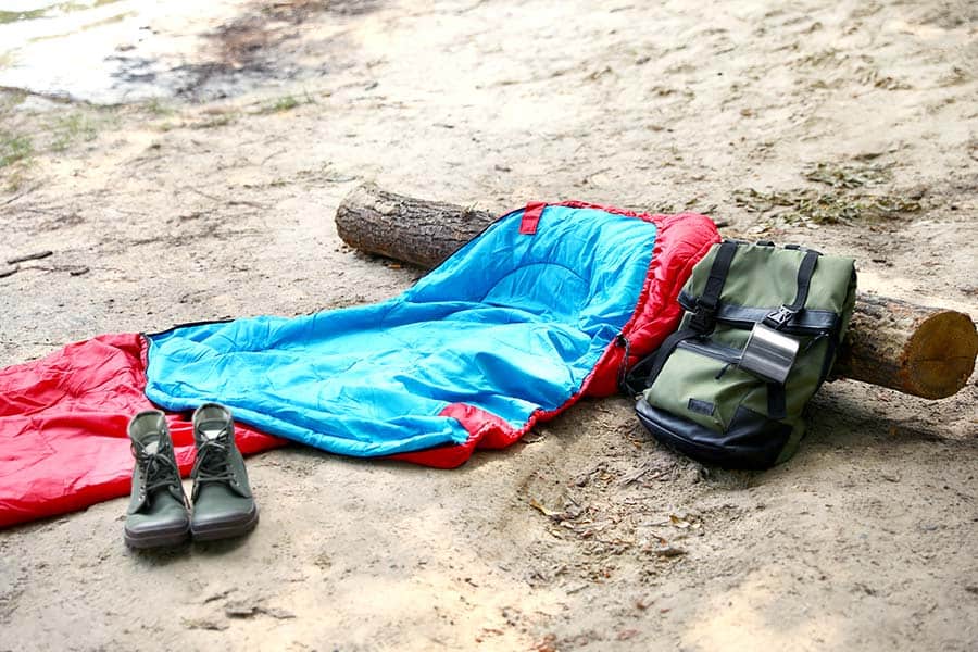 Sleeping bag, backpack and hiking boots on sandy beach