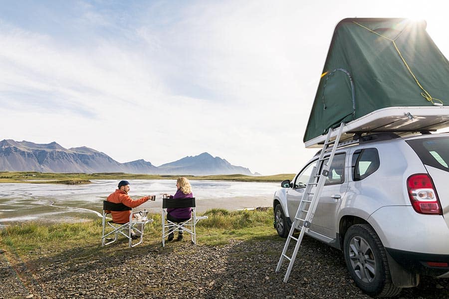 Couple sitting in chairs next to white SUV with rooftop tent