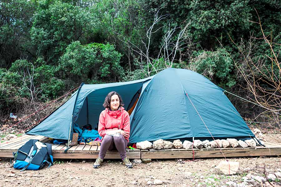 Woman sitting in front of blue tent in the forest