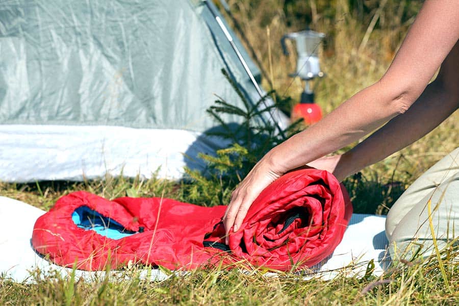 Woman rolling up red sleeping bag by tent