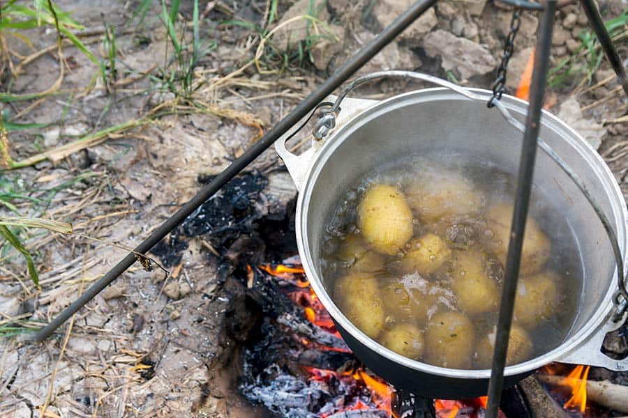 Potatoes boiling in pot over campfire