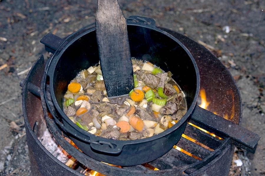 Cooking vegetable stew over campfire