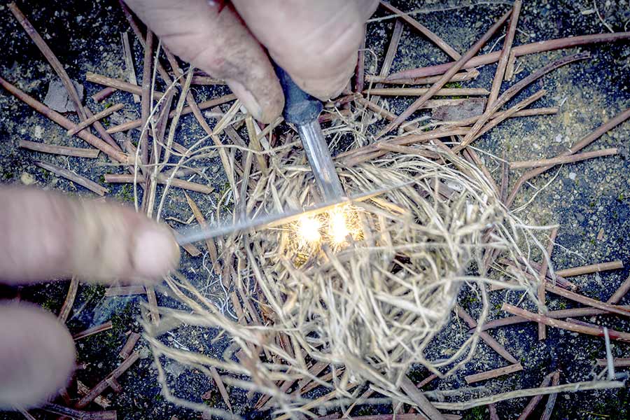 Man using a ferro rod to start a pile of tinder