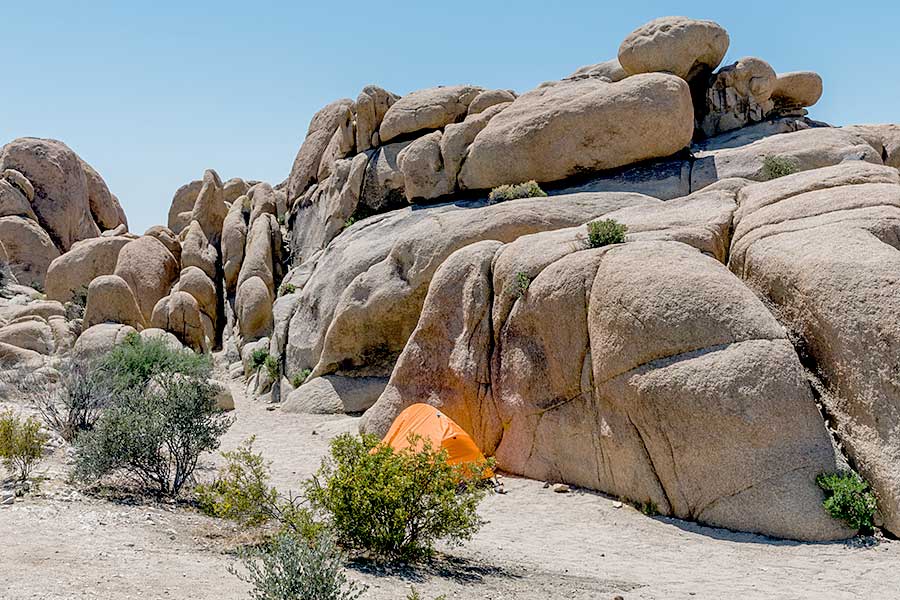 Orange tent pitched a the base of some large boulders