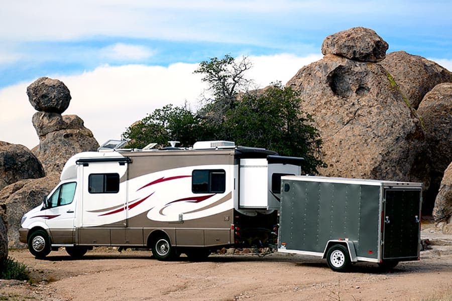 Class C motorhome with cargo trailer parked by boulders